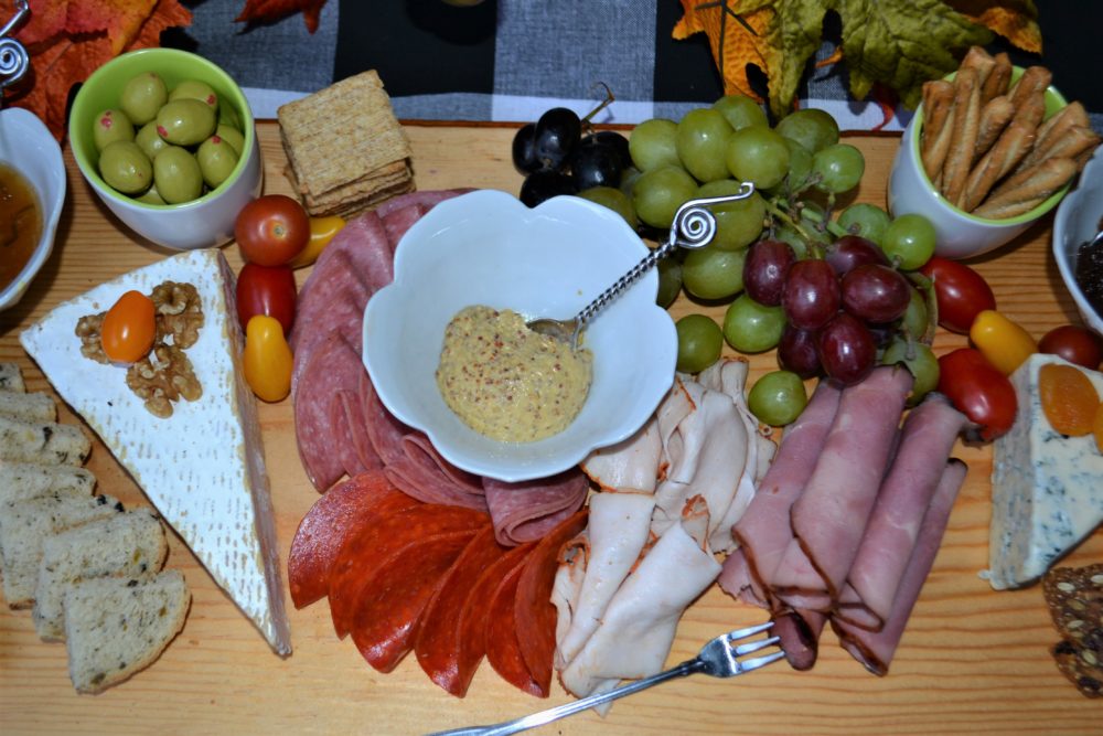 Select a large cutting board –or make one. How to on lizbushong.com Arrange trio of cheese -your choice on board. Arrange fresh fruit   and spreads Nestle assorted crackers & breads that pair with the cheese and spreads Add dried fruits and nuts    